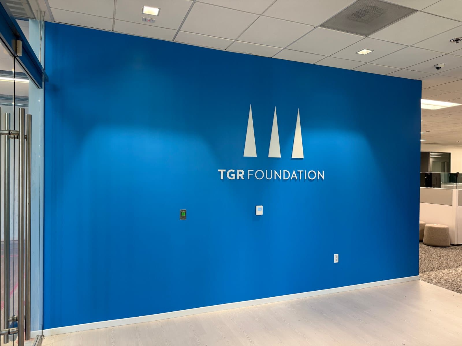 Dimensional white acrylic TGR Foundation logo on a blue lobby wall